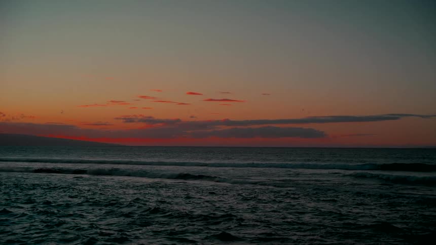 The tranquil ocean glows with the last light of a colorful sunset
