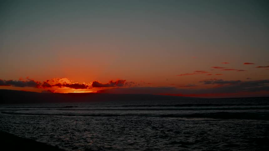 A dramatic orange sunset glows over the horizon as waves gently roll in the ocean