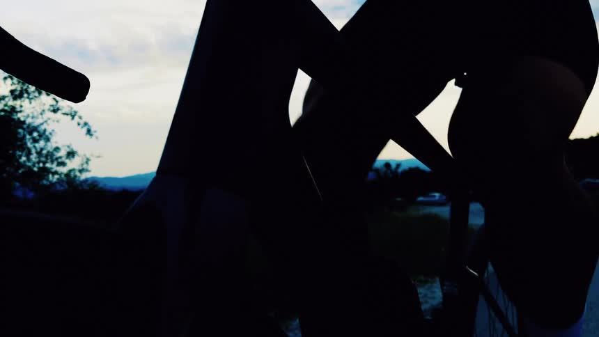 A dynamic low-angle shot captures the silhouette of a cyclist's legs pedaling a road bike at sunset