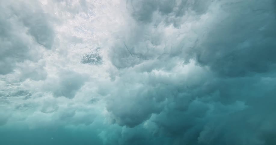 An awe-inspiring underwater slow-motion view shows a massive ocean wave breaking from below