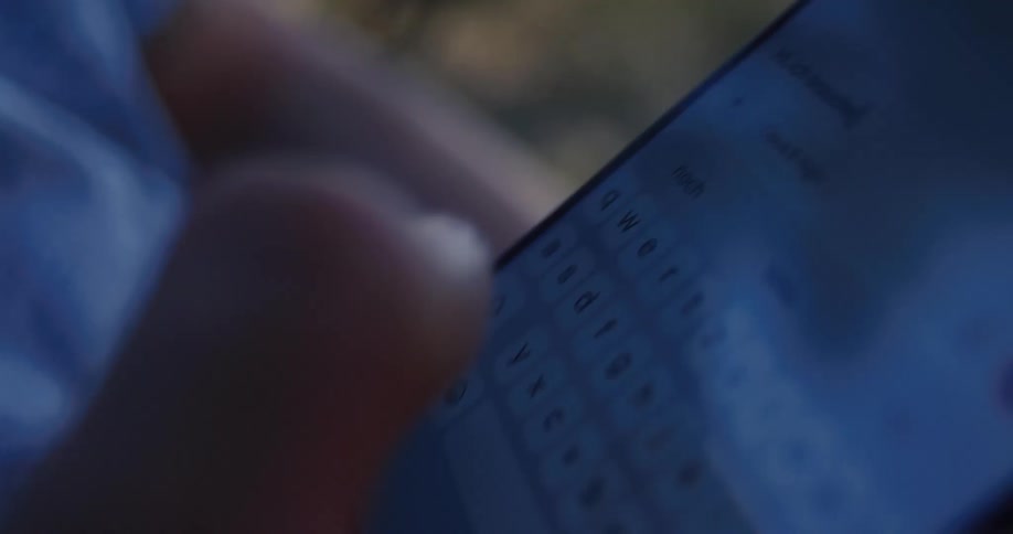 A detailed close-up shot shows a person's fingers typing a message in German on a smartphone screen in low light