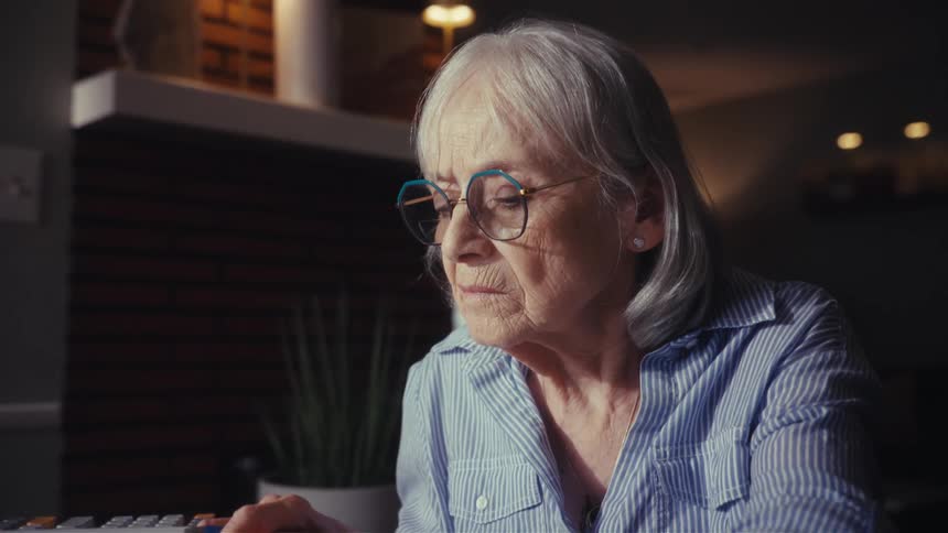 A worried senior woman with glasses contemplates her finances late at night, showing signs of stress and concern