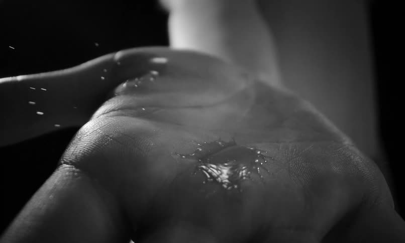 A single droplet of water splashes into the palm of a hand in a dramatic black and white slow-motion close-up