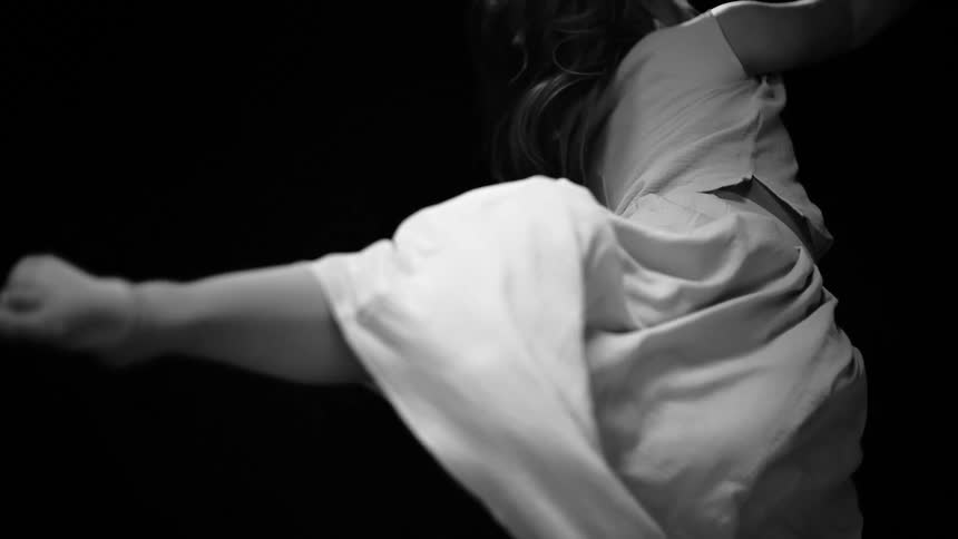 An artistic black and white cinemagraph shows a woman in a flowing white dress frozen in a dynamic dance pose against a dark background