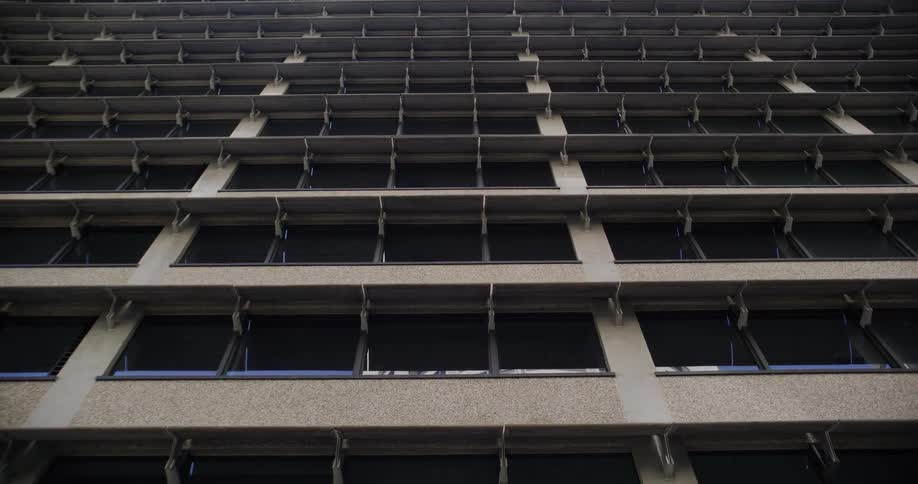 A low-angle static shot of a brutalist concrete office building with a repetitive window pattern