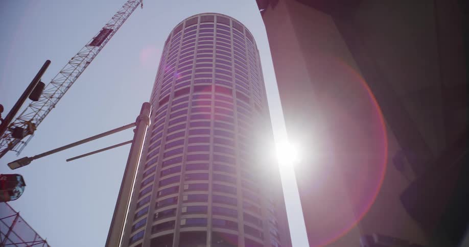 The bright sun emerges from behind a modern cylindrical skyscraper creating a lens flare