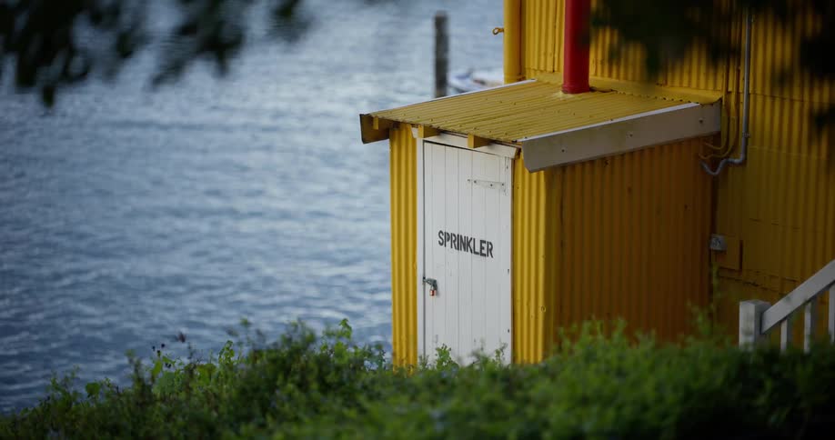 A yellow corrugated metal shed with a sprinkler room door sits next to calm, rippling water