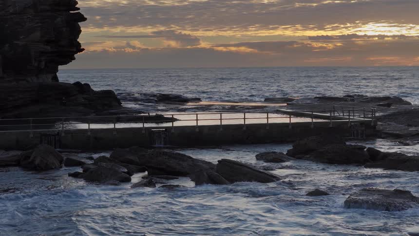 A serene coastal rock pool on a rugged shoreline is continuously filled by the ocean's gentle waves at sunrise