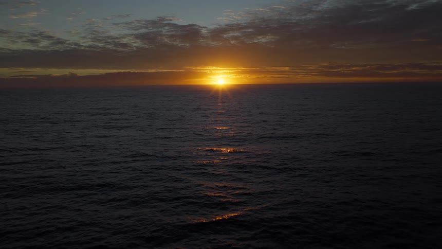 A static, wide shot of the sun setting on the horizon over the vast, dark ocean