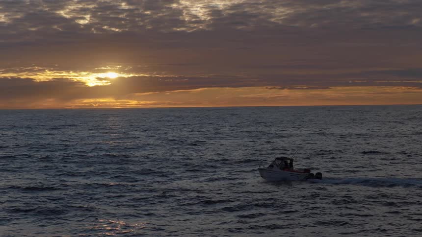 A small fishing boat cruises across the open ocean in slow motion during a spectacular and beautiful sunset