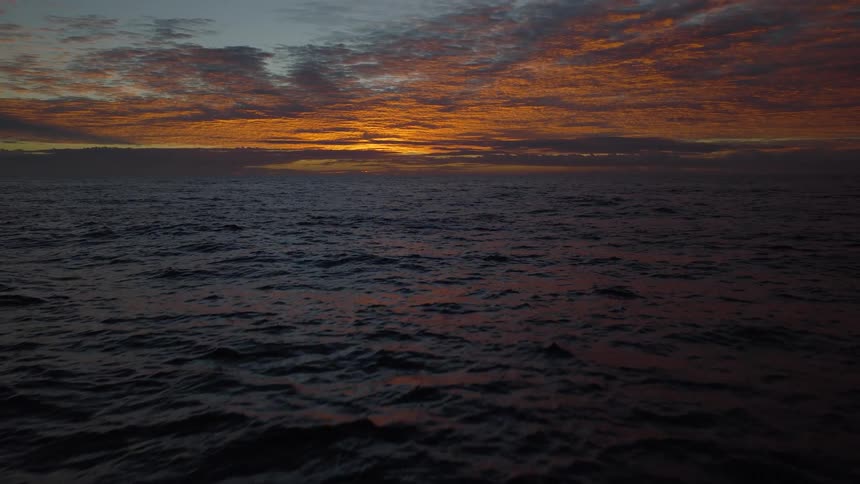 A slow reveal of a breathtaking golden sunset over the dark, rolling waves of the open sea