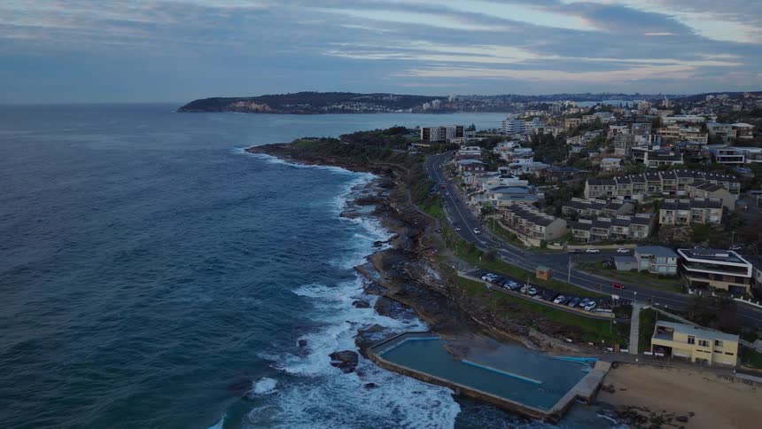 A serene static aerial view of the Queenscliff Rockpool and the surrounding coastline as gentle waves roll in at dusk