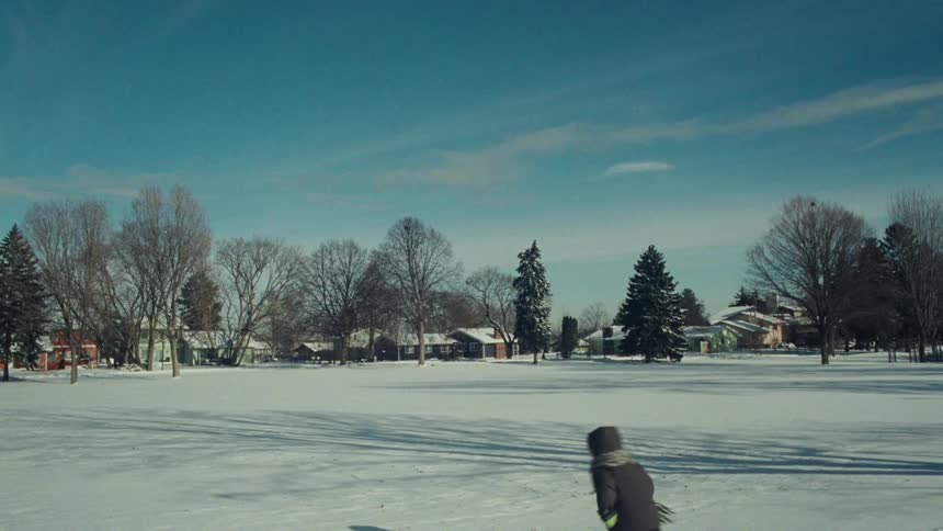 Two young boys in winter coats joyfully run and play in a snow-covered park on a sunny day