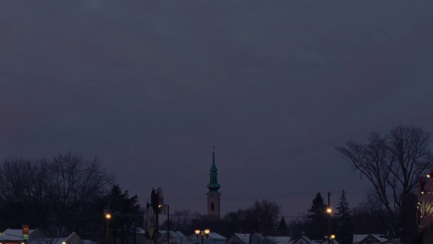 A time-lapse of stars and clouds moving across the sky above a church steeple in a winter town at dusk