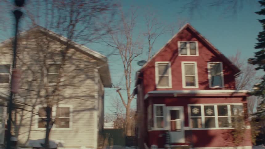 A point-of-view shot driving slowly through a quiet, snow-covered residential neighborhood on a sunny winter day