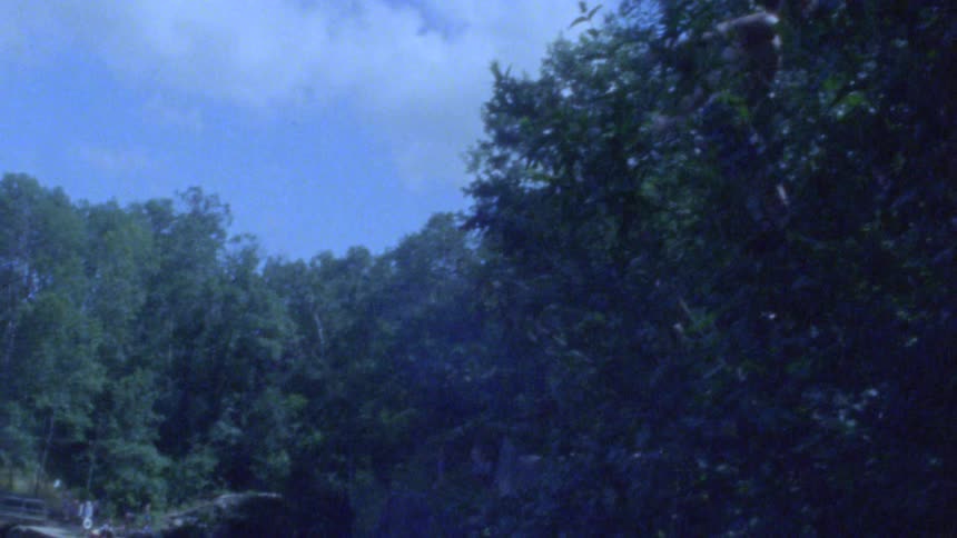 Slow-motion vintage footage captures a daring dive from a tree into a swimming hole surrounded by a forest