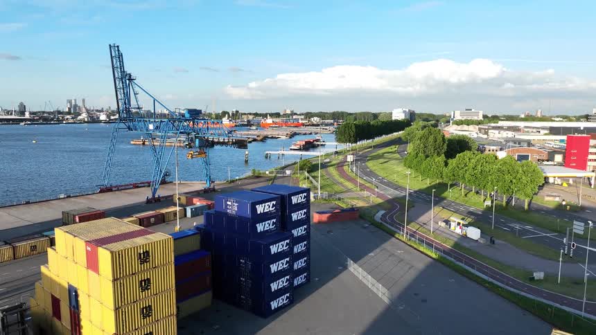 Aerial drone footage flying over colorful shipping containers at an industrial port with a large crane on a sunny day