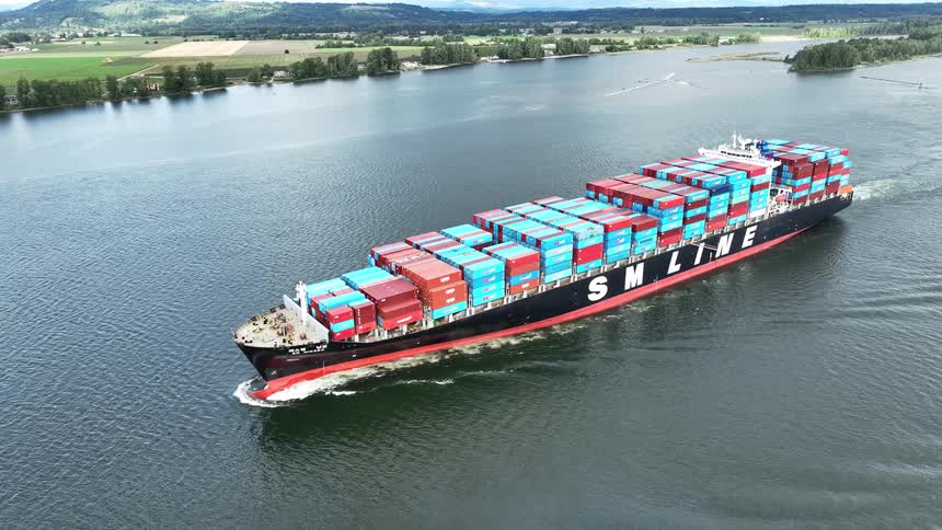 An impressive aerial view captures a massive container cargo ship as it sails along a wide river, flanked by green countryside