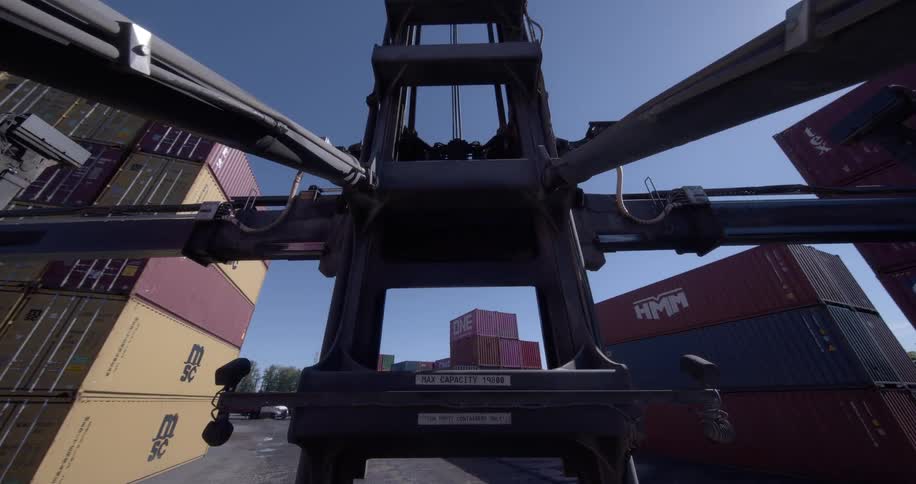 A point-of-view shot from a container handler reversing through an industrial shipping yard on a sunny day