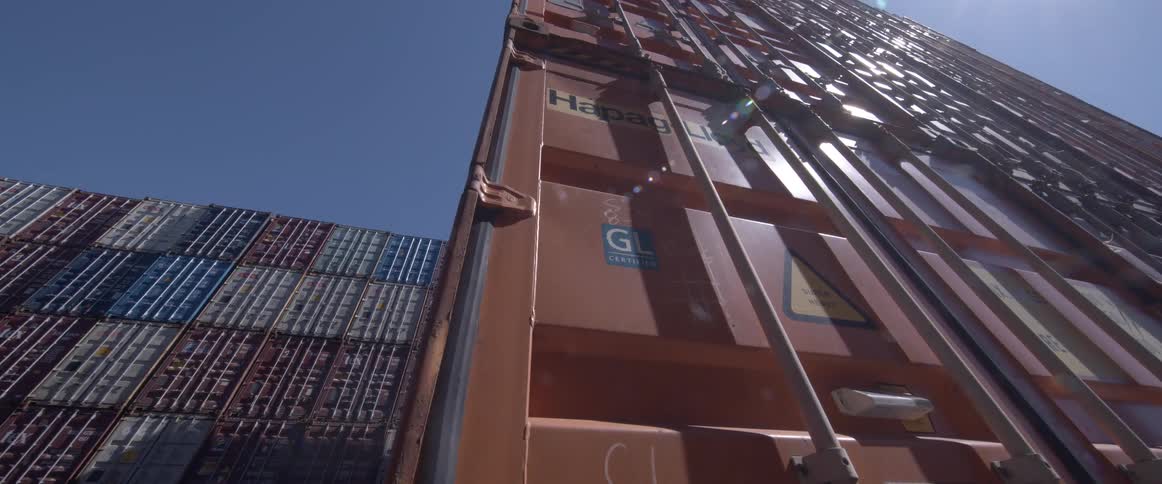 Low angle shot of a large orange shipping container in a port yard under a bright, sunny sky