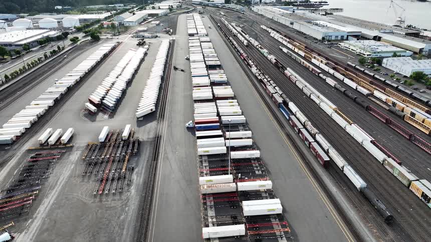 Expansive aerial view of a bustling industrial railyard with rows of shipping containers and long freight trains waiting for transport