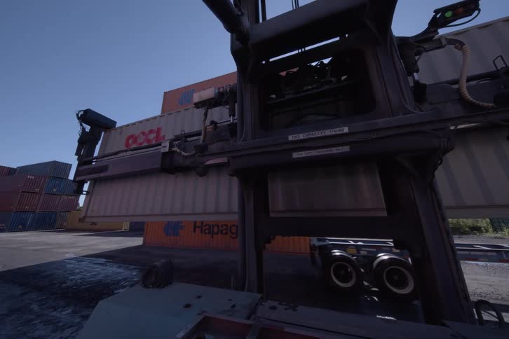 POV from a reach stacker as it lifts a large shipping container off a truck and moves through a sunny industrial port
