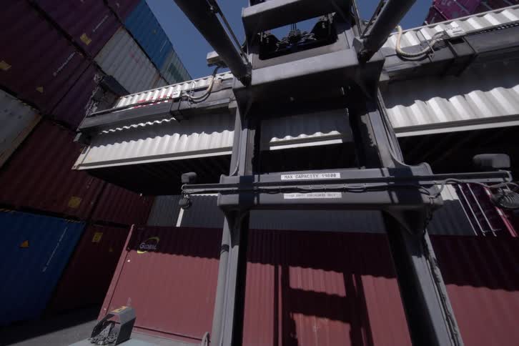 POV from a forklift as it maneuvers and stacks a large shipping container in a busy industrial port yard