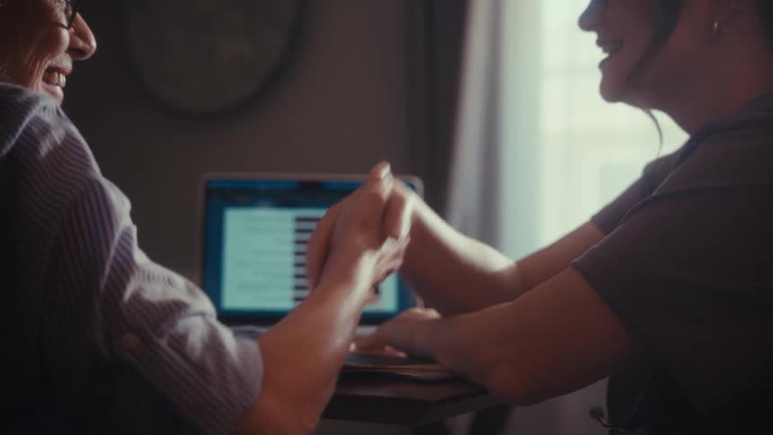 A caring nurse holds an elderly patient's hand and then shakes it in a supportive gesture during a home consultation