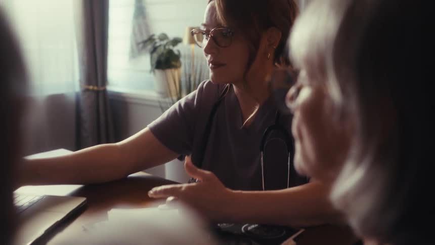 A compassionate healthcare worker discusses medical information with a senior couple in a sunlit room