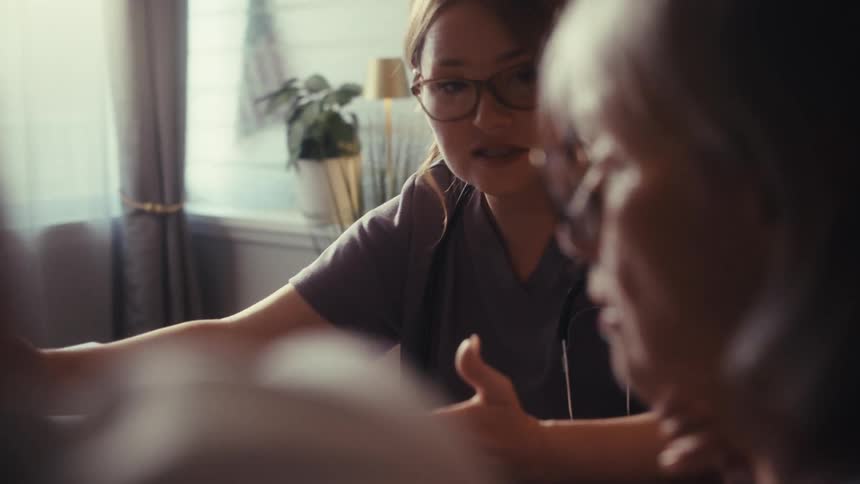 A compassionate doctor explains medical statistics on a laptop to an elderly couple during a home visit
