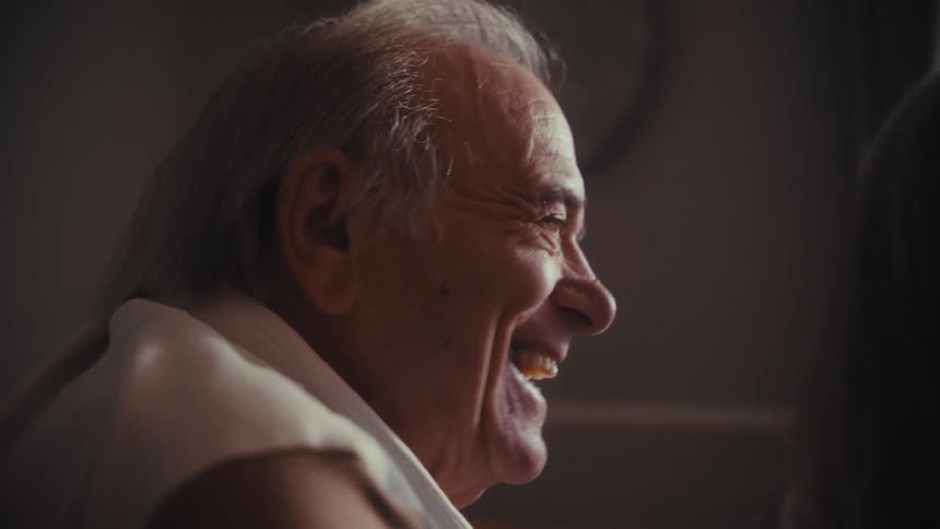 A joyous elderly man with gray hair shares a laugh during a warm, intimate conversation in slow motion
