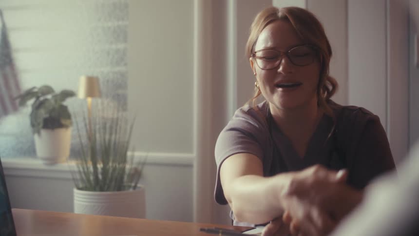 A friendly nurse smiles and laughs while talking with a patient during a consultation, ending with a reassuring handshake