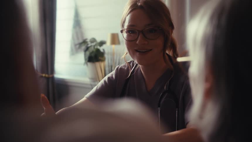 A caring female doctor explains medical results from a laptop to an elderly couple during a warm and friendly home consultation