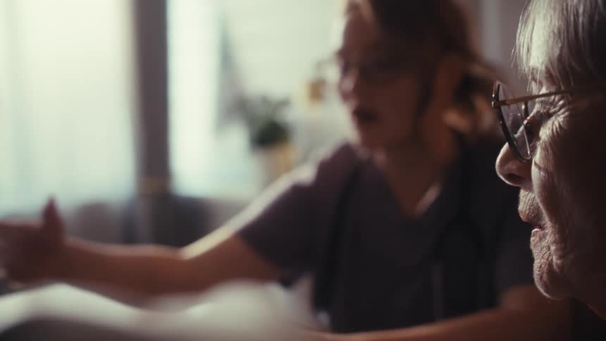 A caring female doctor explains medical statistics on a laptop to her elderly patient during a consultation at home
