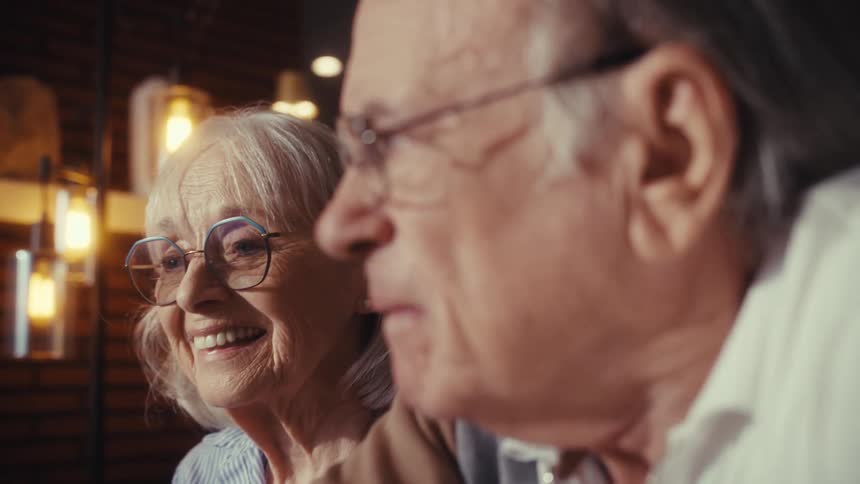 An elderly woman with glasses laughs joyfully next to her husband in a warm and cozy slow-motion scene