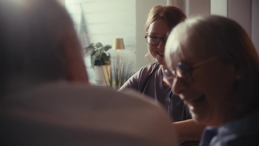 A caring female nurse smiles warmly as she shares good news with an elderly couple, bringing them comfort and laughter