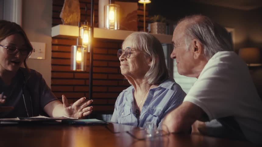 A female nurse provides an in-home consultation for an elderly couple at their dining table