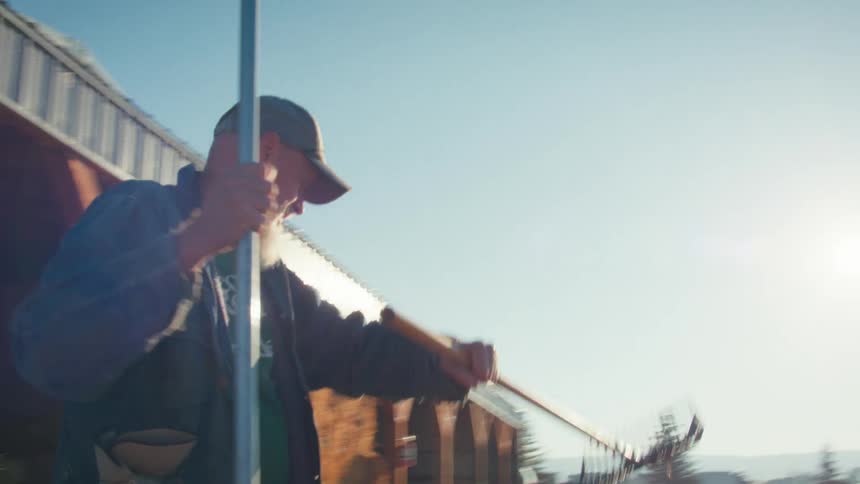 A farmer grabs a rake from a hay barn and walks out into the bright sunlight to begin his work day