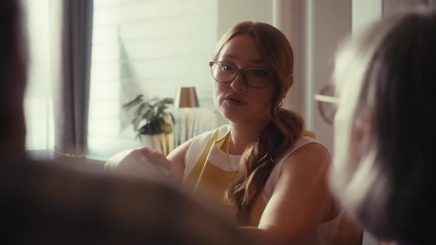 Over the shoulder shot of a female professional with glasses and a yellow top talking and gesturing during a meeting
