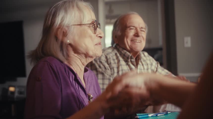 A delighted senior couple celebrates sealing a deal by shaking hands with an advisor in their home