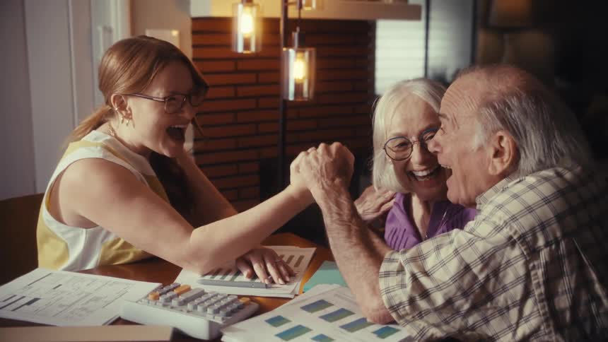 A financial advisor and an elderly couple celebrate a successful financial planning meeting with a playful arm wrestling match