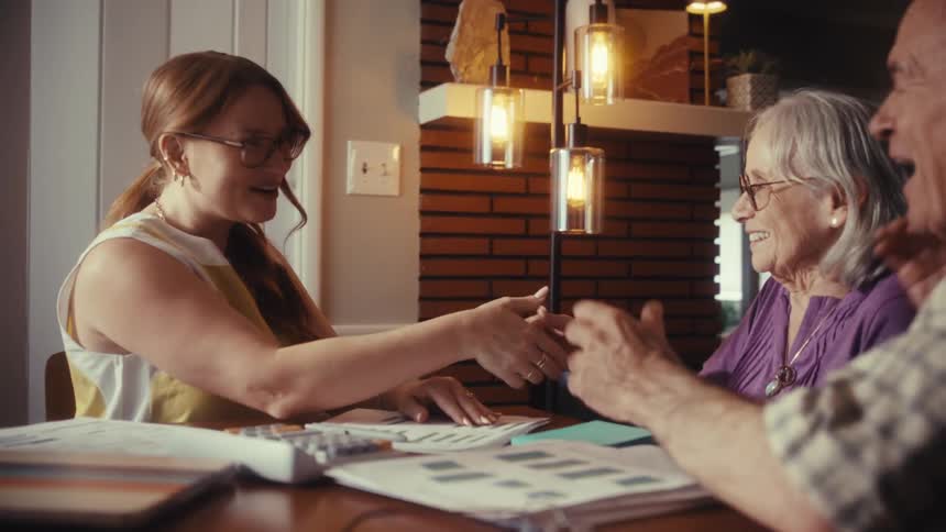 A female advisor shares positive financial results with a senior couple, ending with a joyful handshake and hug