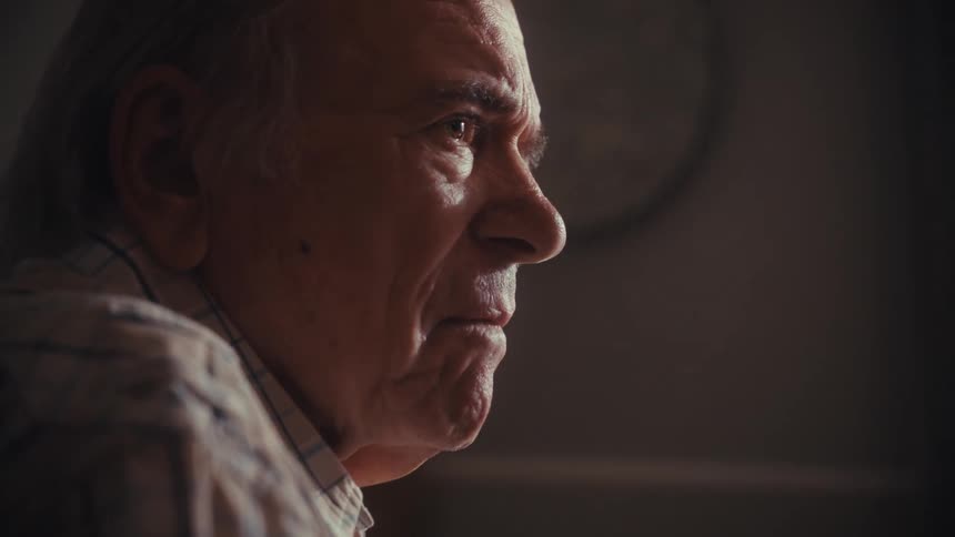 Dramatic close-up of a contemplative senior man's face in profile, lost in thought or memory