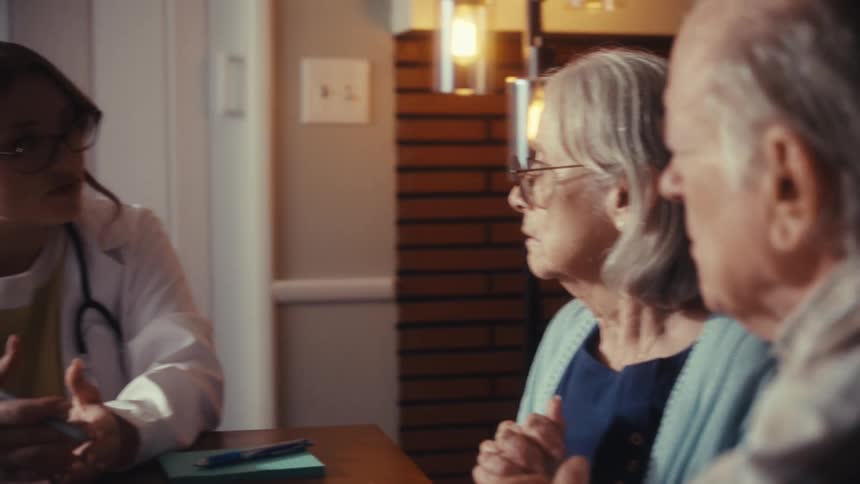 A concerned senior couple listens as their doctor explains medical results during a home visit