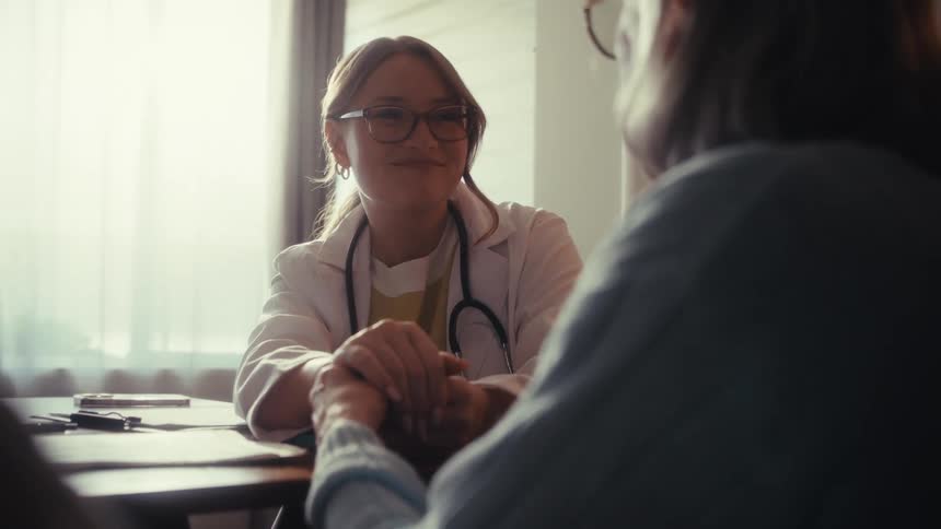 A compassionate female doctor offers support and reassurance to an elderly patient by holding her hand during a home visit
