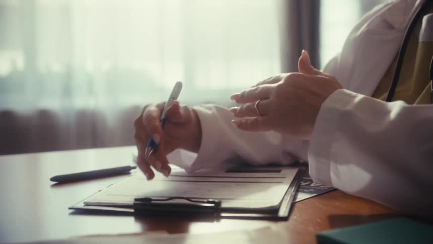 Close-up on a doctor's hands as they gesture with a pen while explaining a diagnosis to a patient in their office