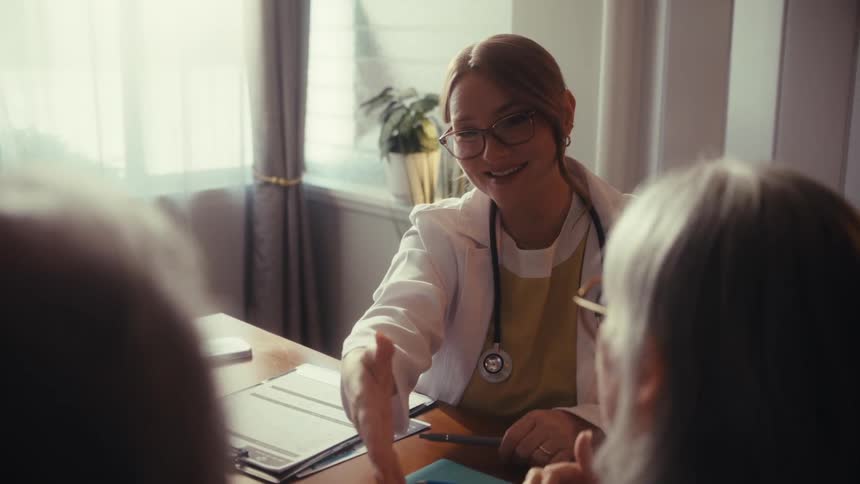 A friendly female doctor shakes hands with an elderly couple after a positive consultation in her office