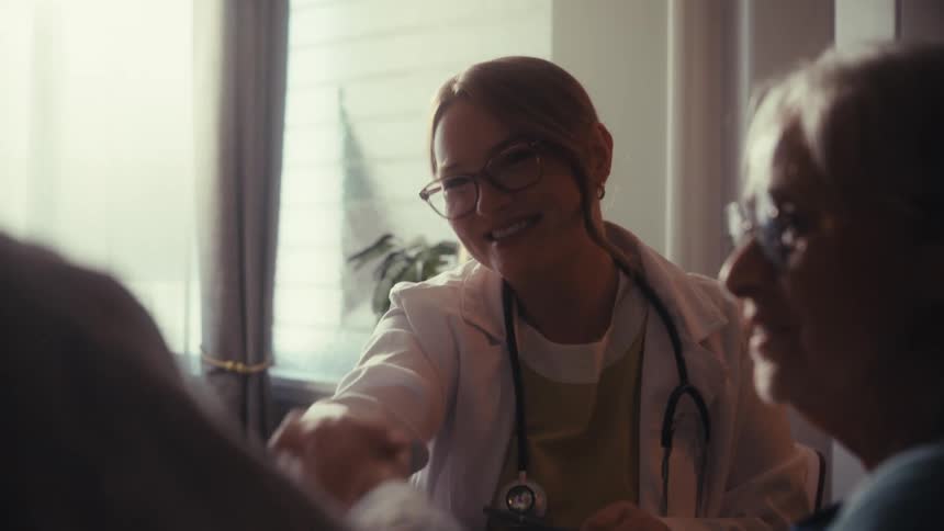 A friendly female doctor smiles warmly as she consults with and reassures an elderly couple in her sunlit office