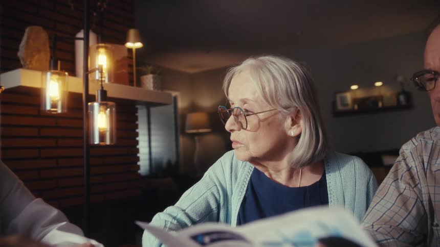 A female doctor consults with a senior couple in their home, with the camera slowly zooming in on the woman's concerned face