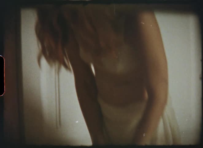 An intimate, voyeuristic shot on vintage film of a woman in a white slip putting on her stockings in a bedroom